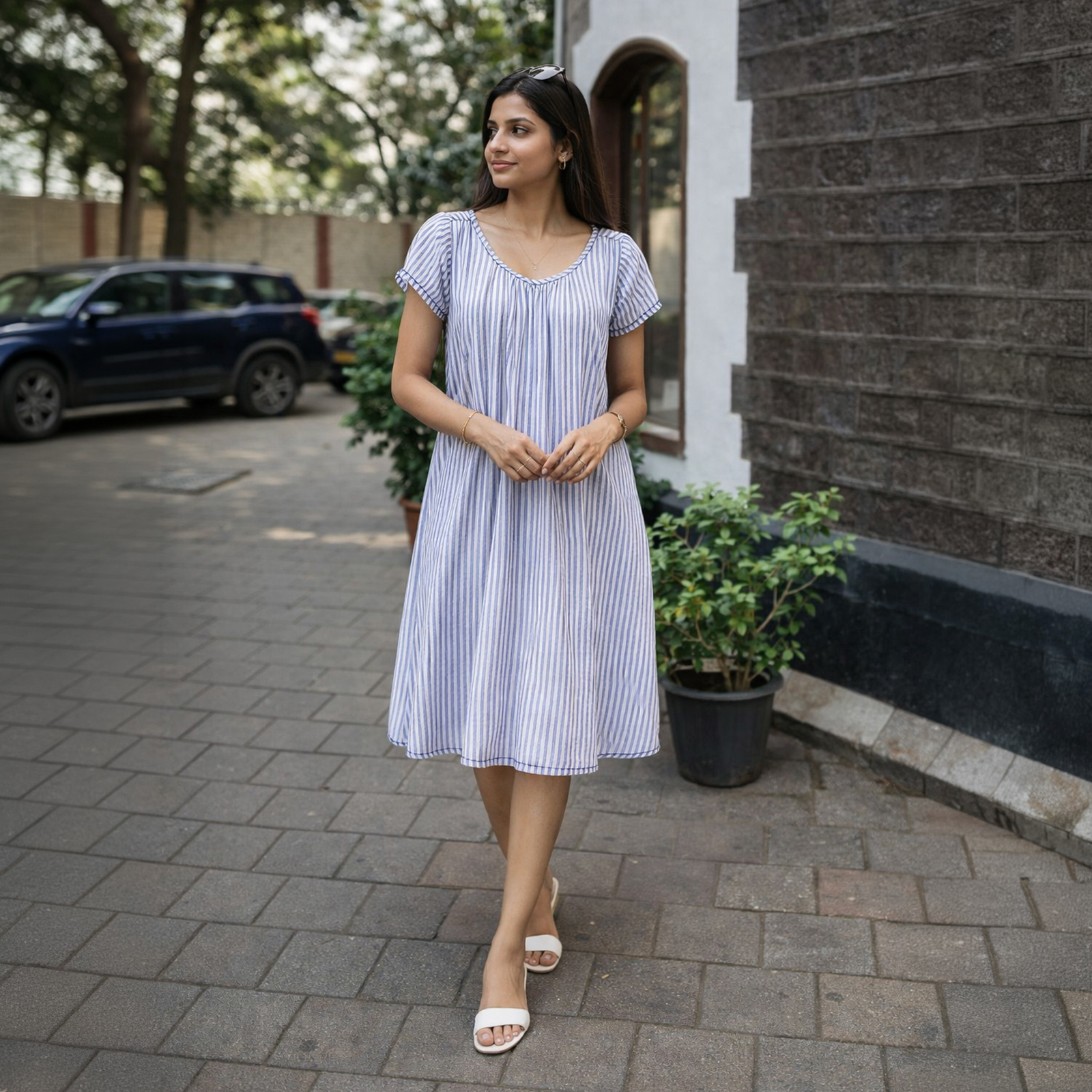 Woman in a bluewhite striped midi dress walking on a sidewalk beside a brick building